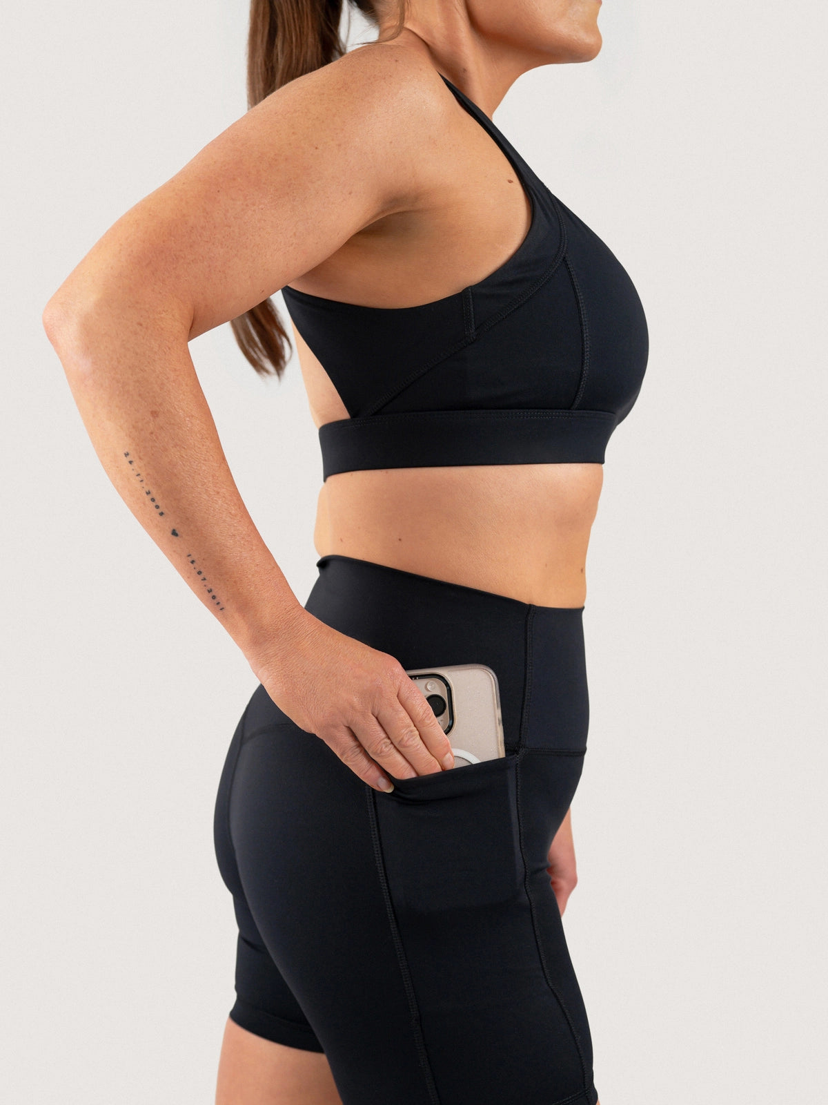 Side view of the Aella Storm Hybrid Shorts in Black with a
phone in the side pocket.
